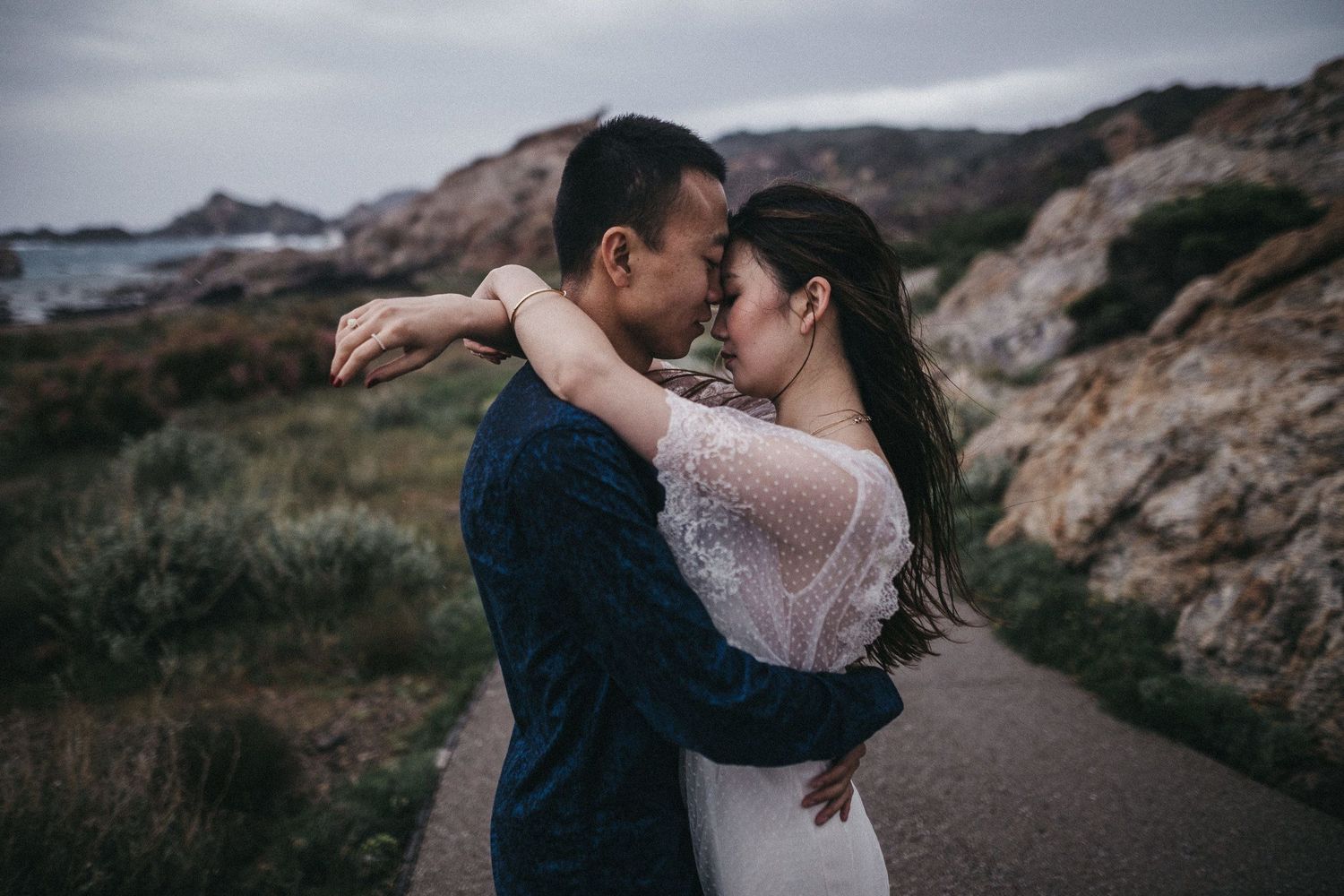 Romantic embrace on a seaside path with dramatic coastal scenery.
