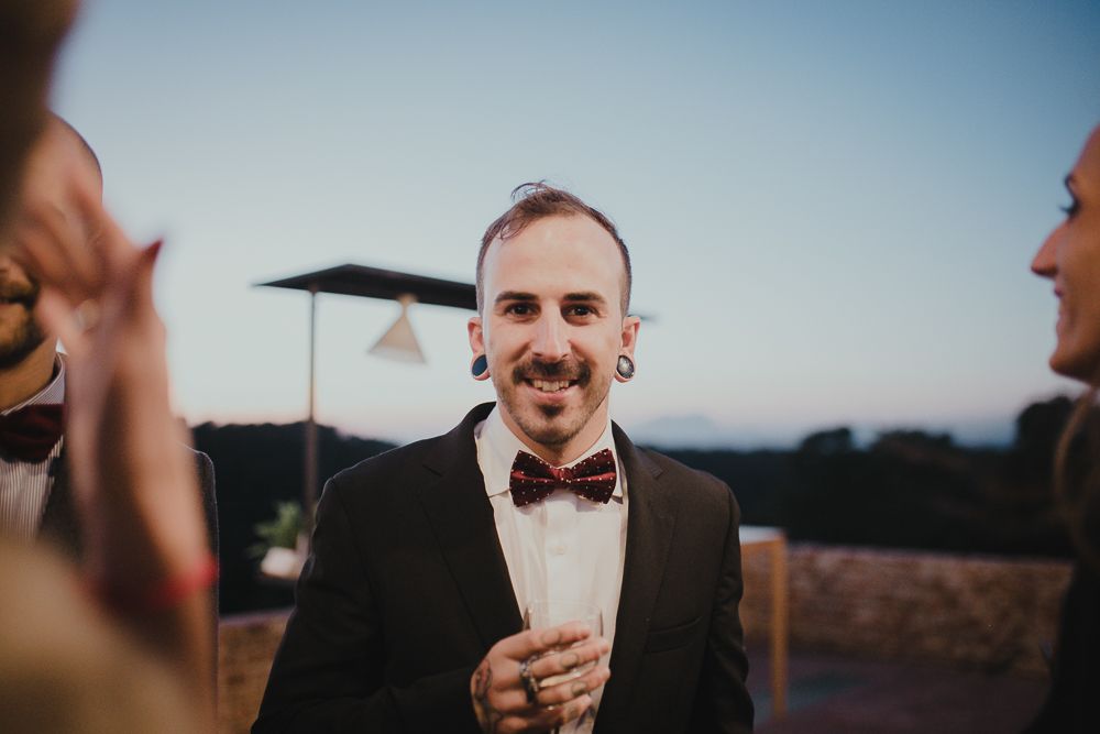 At an outdoor evening event, someone in a black tuxedo and bowtie stands conversing with others.