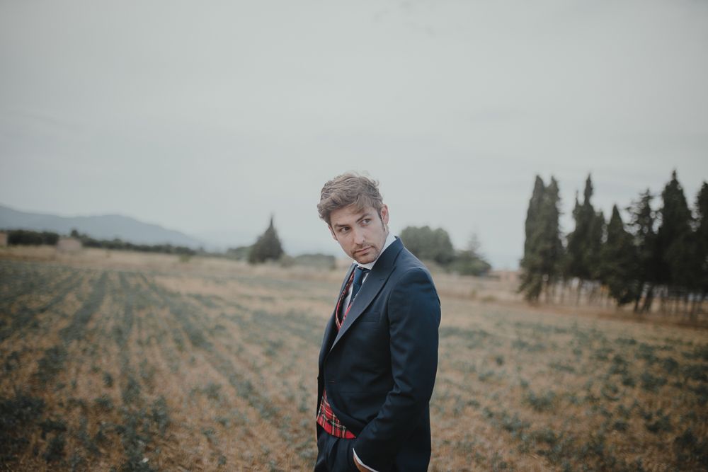 Figure in navy suit standing in rural landscape with mountains in background.