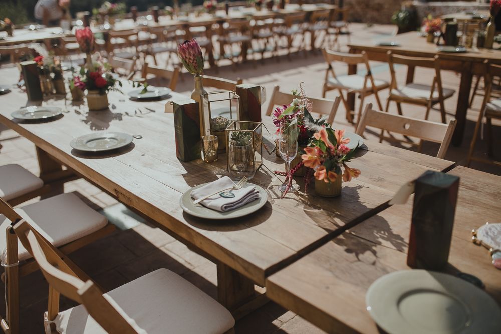 Rustic wedding reception table setup with wooden tables, place settings and floral centerpieces.