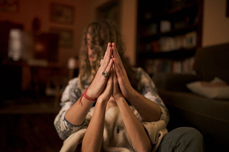 Two people press their palms together while sitting on a couch in a softly lit room.