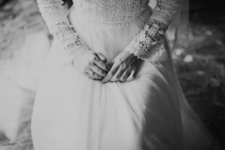 Black and white detail shot of bride's hands resting on lace wedding dress.