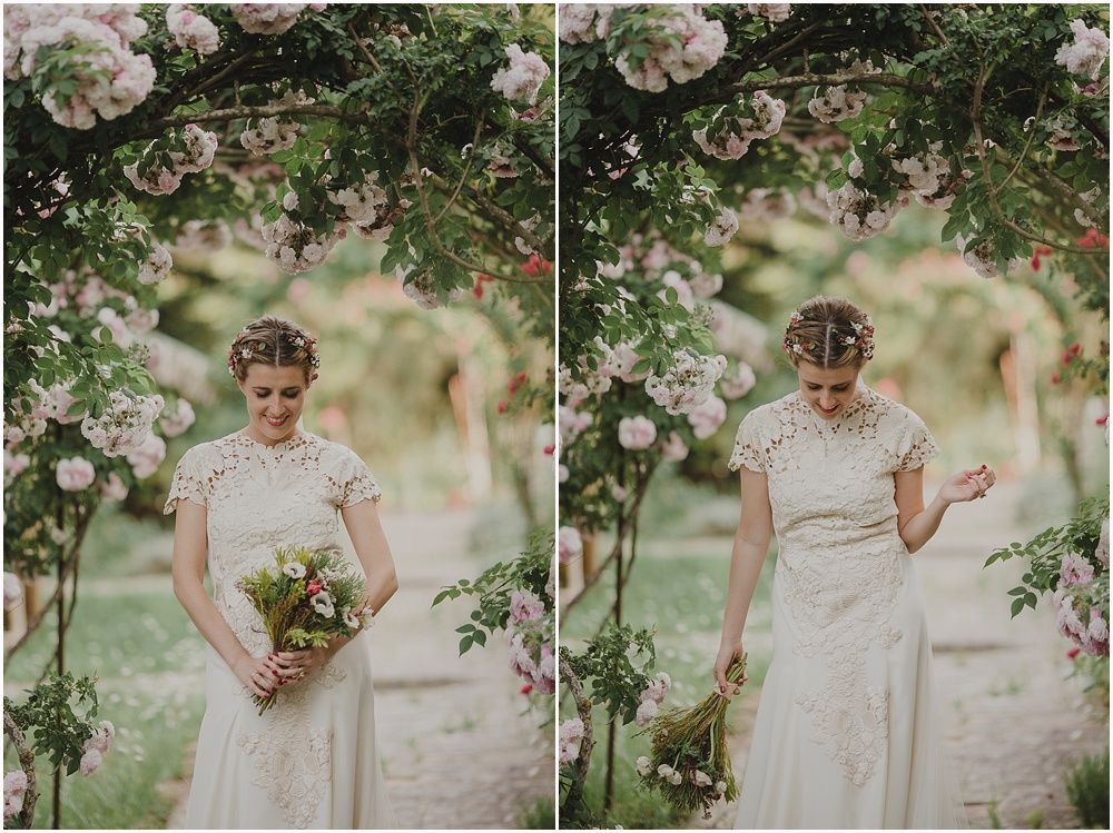 A vintage-style bride poses under flowering branches in a garden setting.