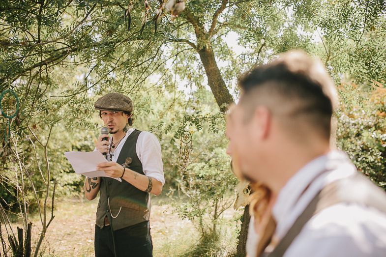 Wedding officiant in vintage attire reads ceremony notes in a sunlit garden setting.