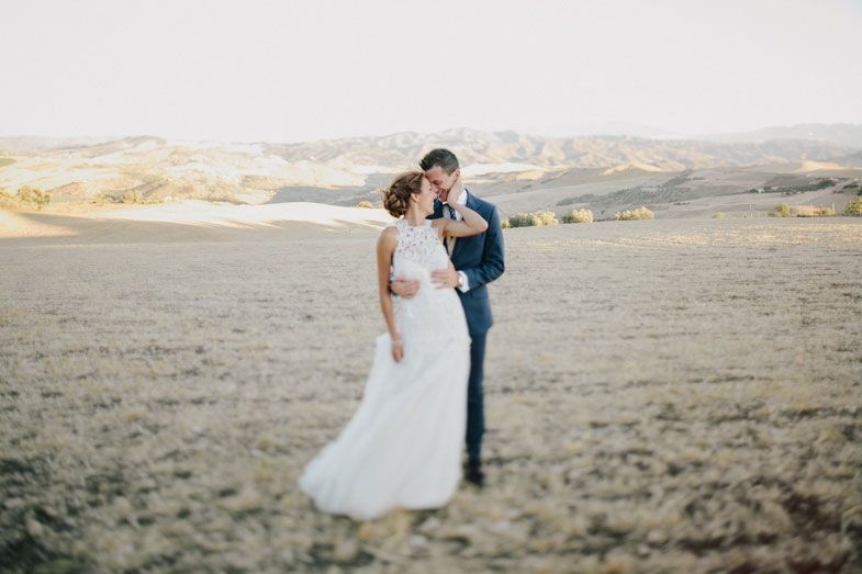 Intimate moment between newlyweds in rustic Italian landscape setting.