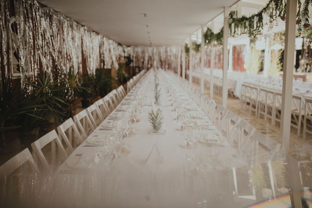 Long elegant wedding reception table decorated with hanging florals and white linens in an indoor venue.
