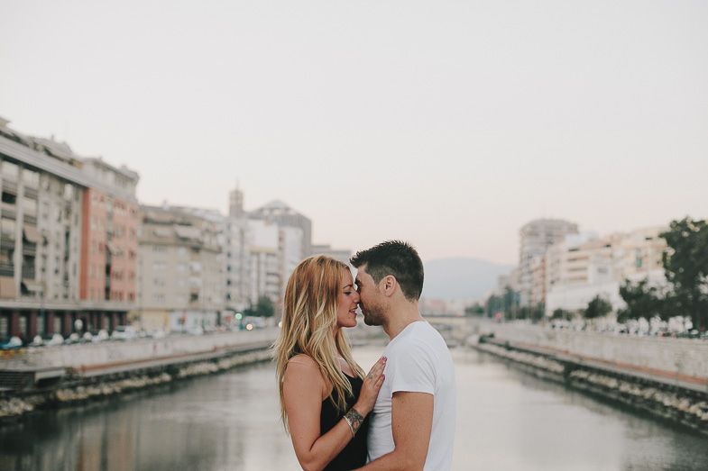 A tender romantic moment between a couple standing by an urban waterway at dusk.