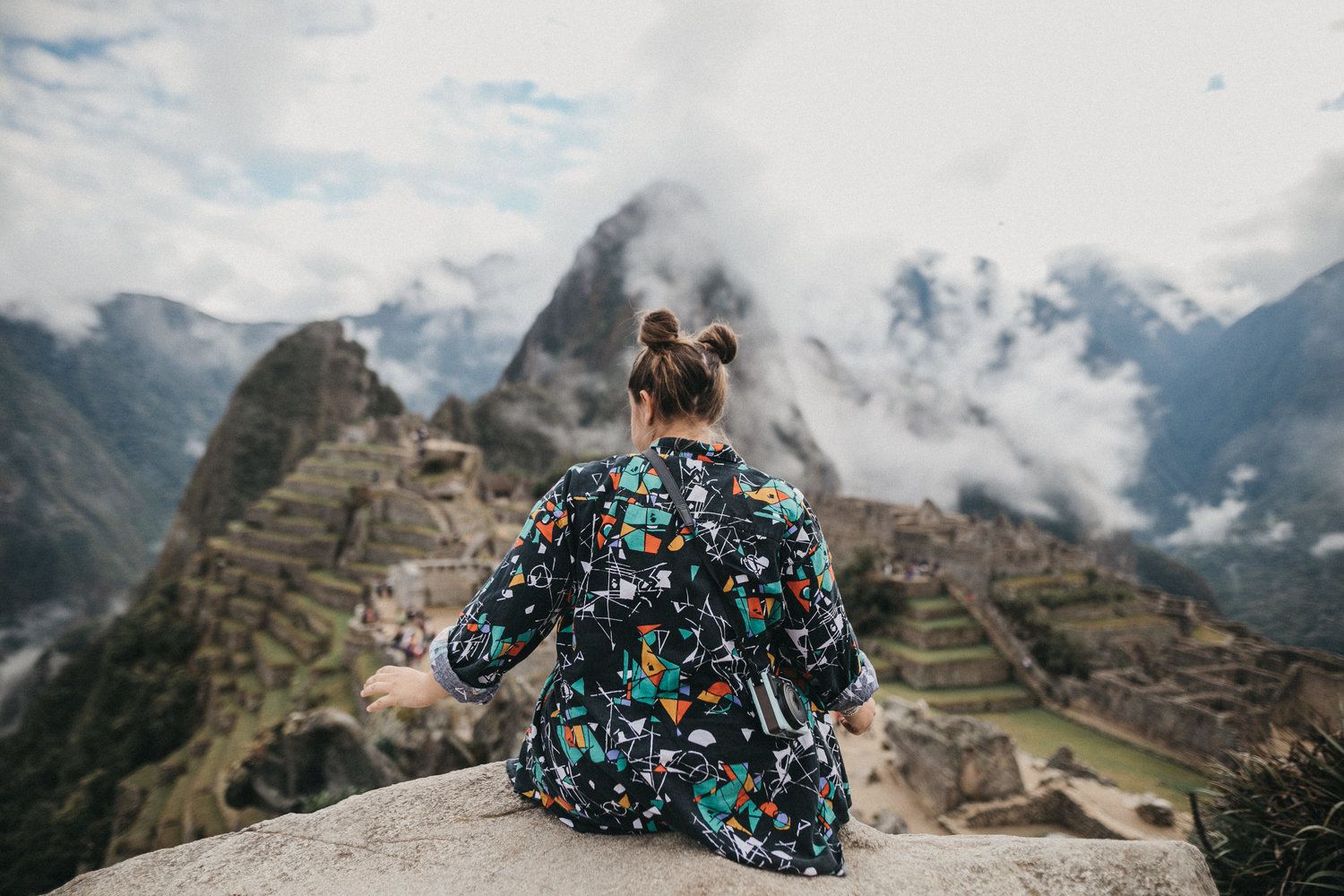 Person in floral dress overlooking the mystical ruins of Machu Picchu surrounded by misty mountains.