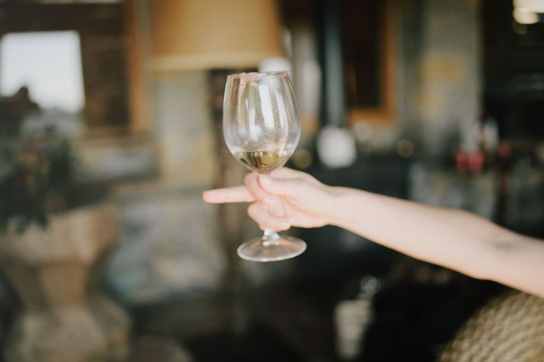 A hand holds a wine glass against a blurred interior background.