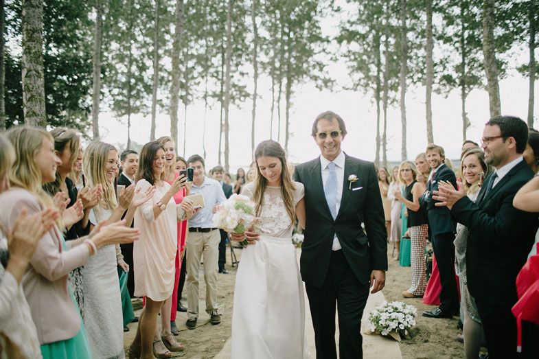 Wedding couple walks through cheering guests in a beautiful forest setting.
