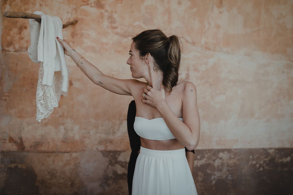 Someone in a white two-piece outfit examines clothing on a vintage textured wall.