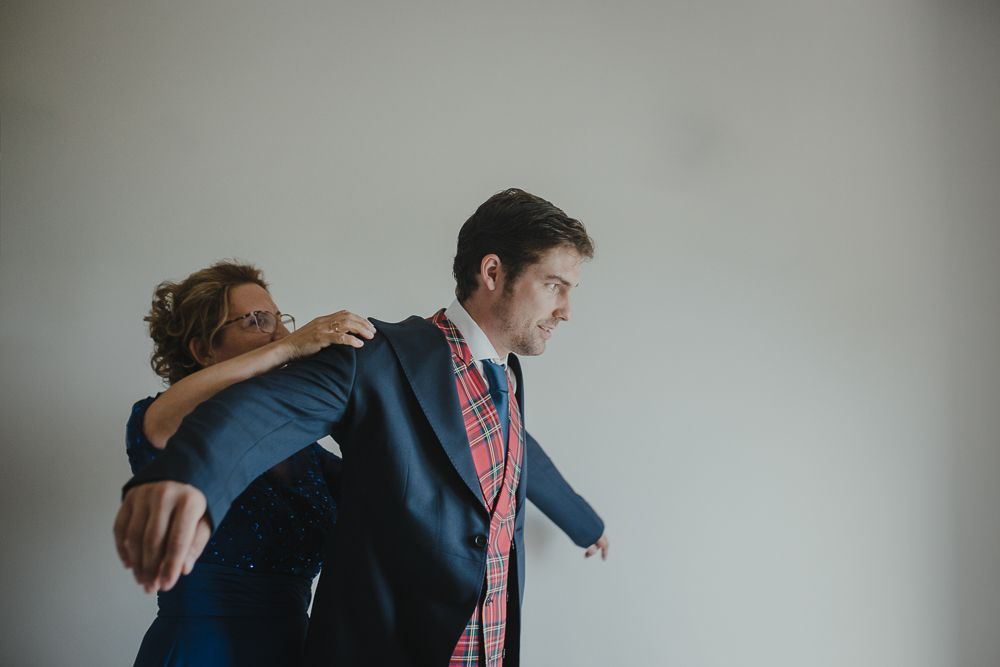 Two people embracing in formal attire against white wall.