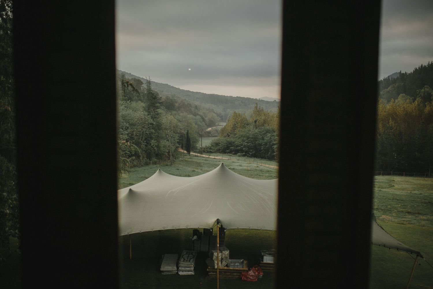 View through window shows event tent setup in rolling countryside.