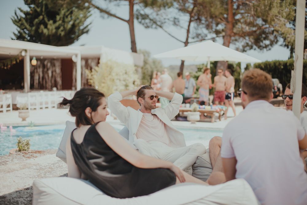 Guests relaxing on cushions by a pool at an outdoor summer party.