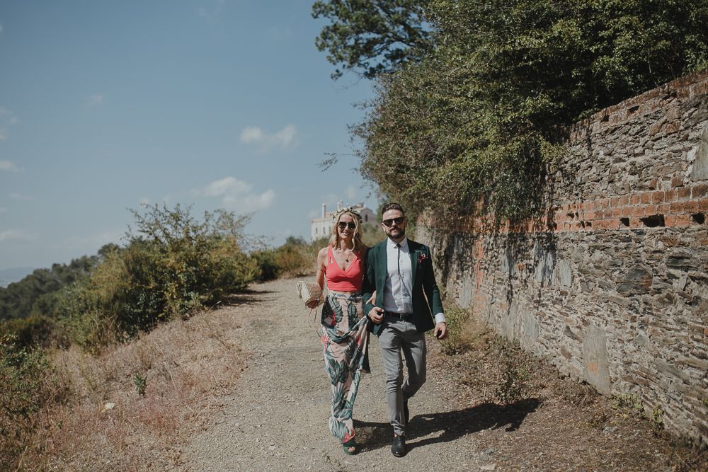 Couple walking along a scenic mountain path next to an old stone wall.