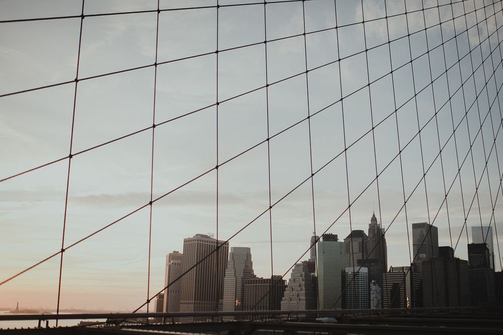 Manhattan skyline viewed through geometric bridge cables at sunset.