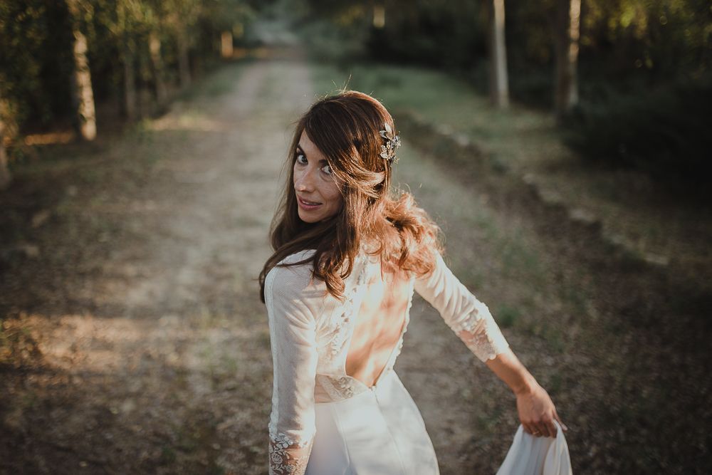 A bride in a long-sleeved white dress twirls on a forest path surrounded by autumn trees.