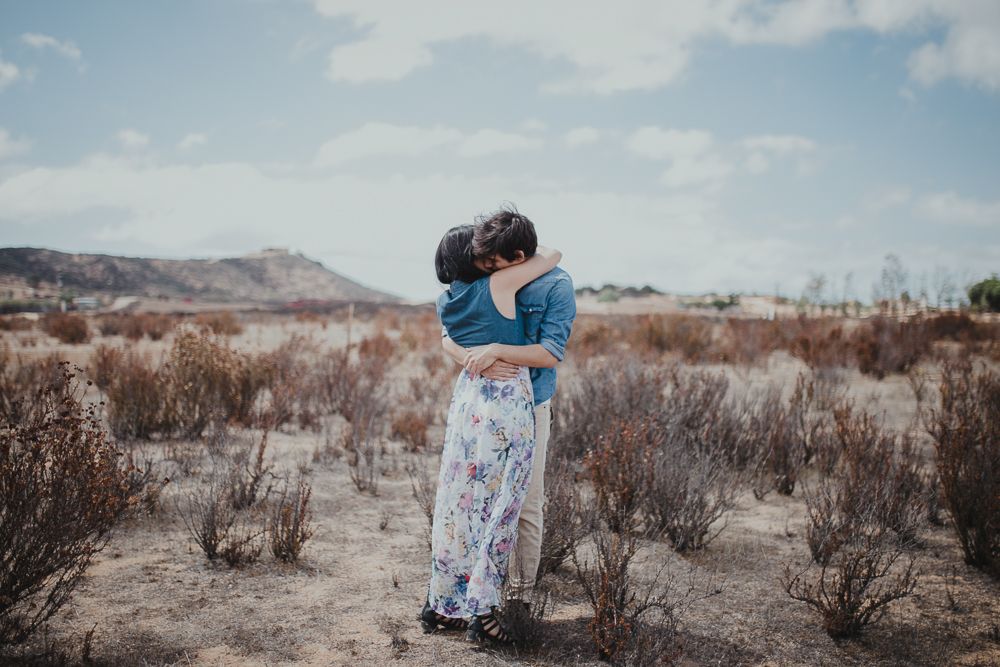 Two people share a tender embrace in a desert landscape under blue skies.