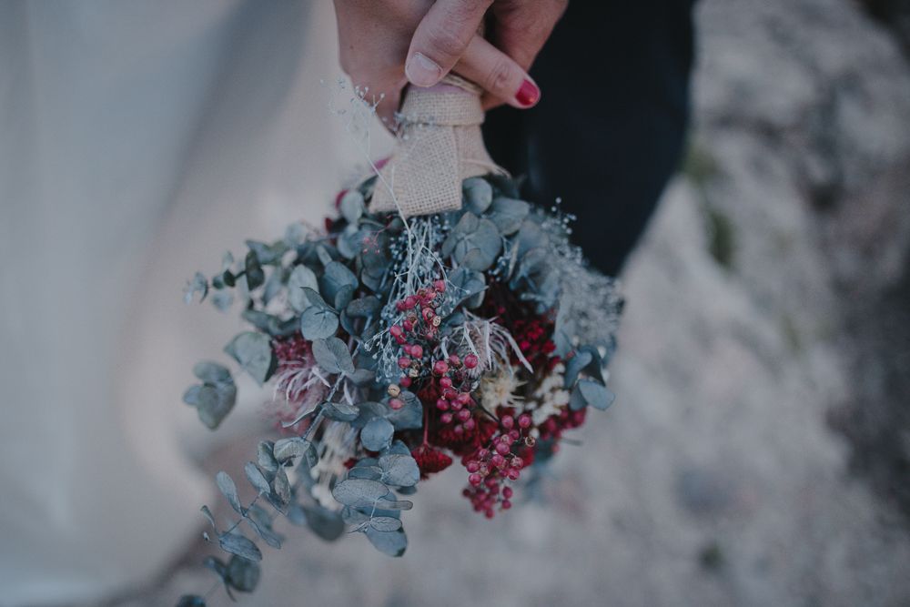 Delicate bouquet with blue eucalyptus and pink flowers held against white fabric.