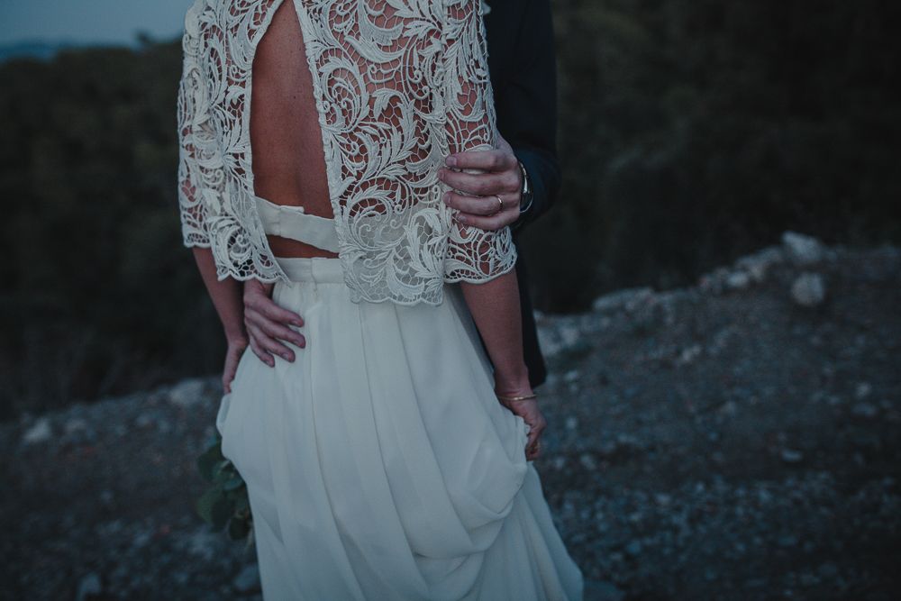 Close-up detail of a bride's lace wedding dress bodice against mountain scenery.