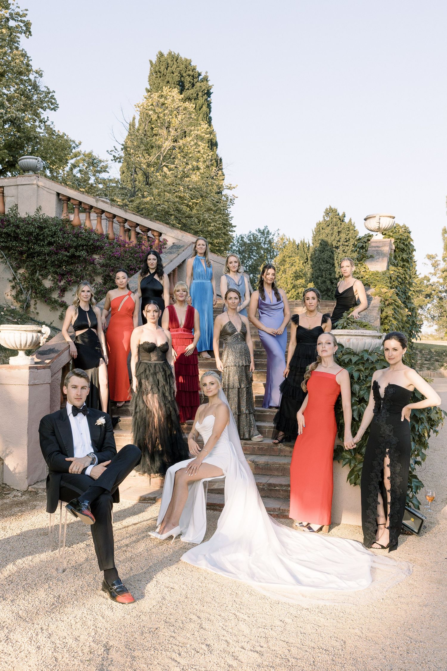 Wedding party posed on elegant stone staircase with bridal gown and colorful formal dresses.