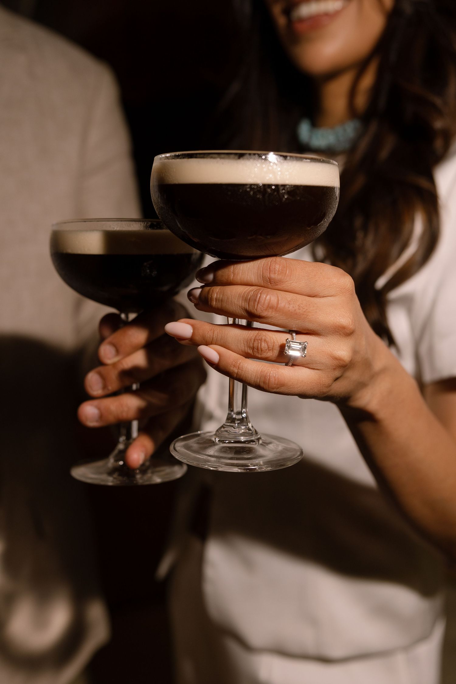 Close-up of two cocktail glasses held by Elina and Jag, with Elina’s ring visible.