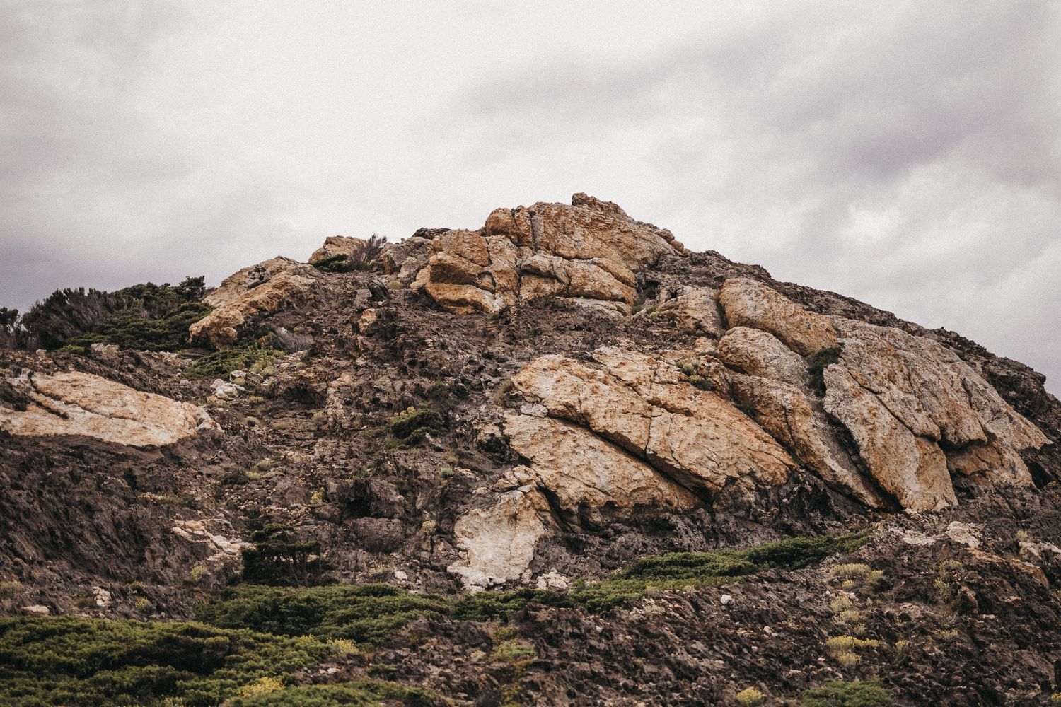 A dramatic rocky mountain formation rises against cloudy skies in a desert landscape.
