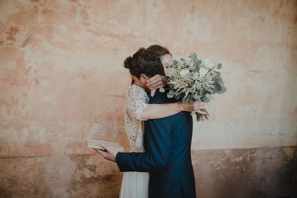 Newlyweds embrace against a peach-colored wall during their wedding.