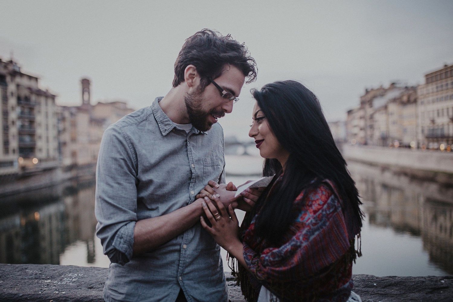 Couple looks at each other lovingly while standing on a bridge in Florence, Italy.