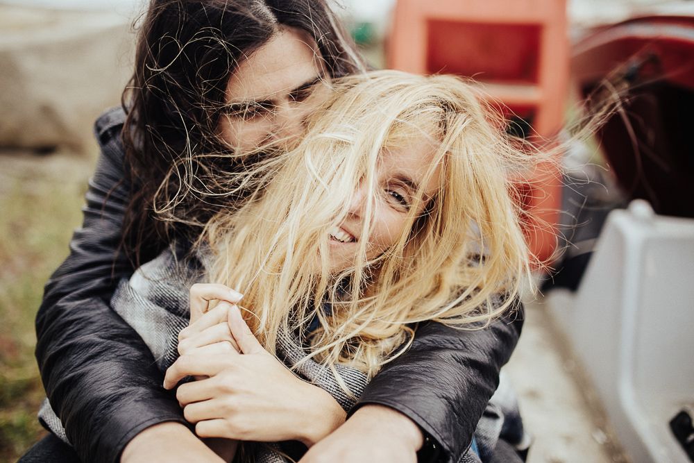Two people share a playful moment with windblown hair outdoors.