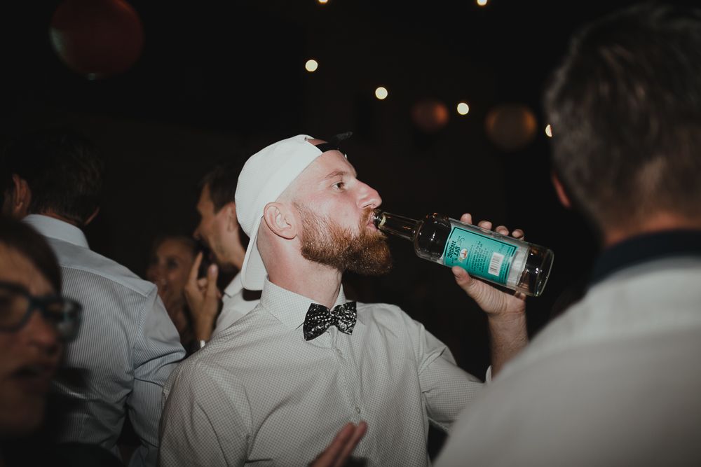 Wedding guest takes a celebratory drink from a bottle during a dark reception party.