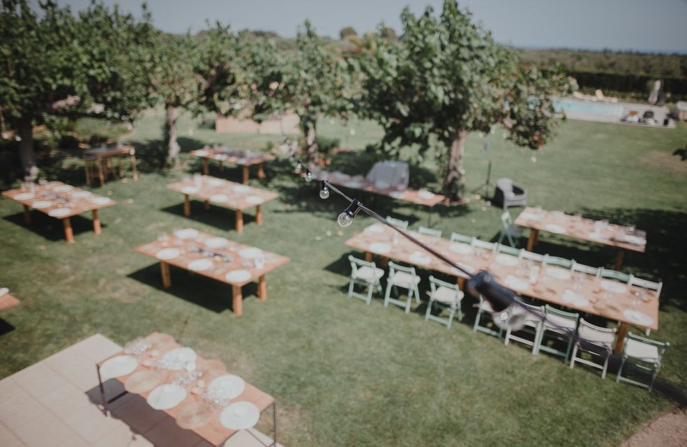 Aerial view of outdoor wedding reception setup with rustic wooden tables on grass.