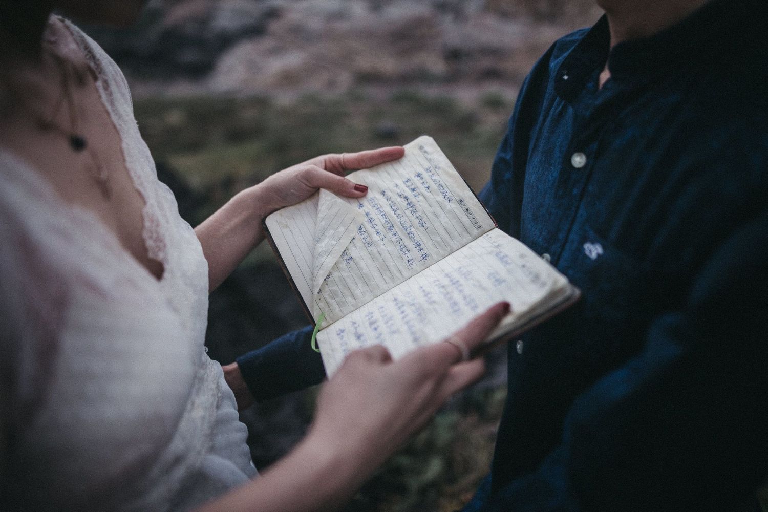 Two people holding and reading from a handwritten book or journal outdoors.