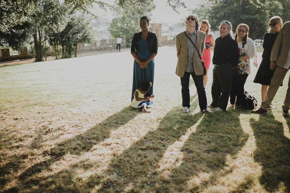 Group of wedding guests casting long shadows on grass in afternoon light.