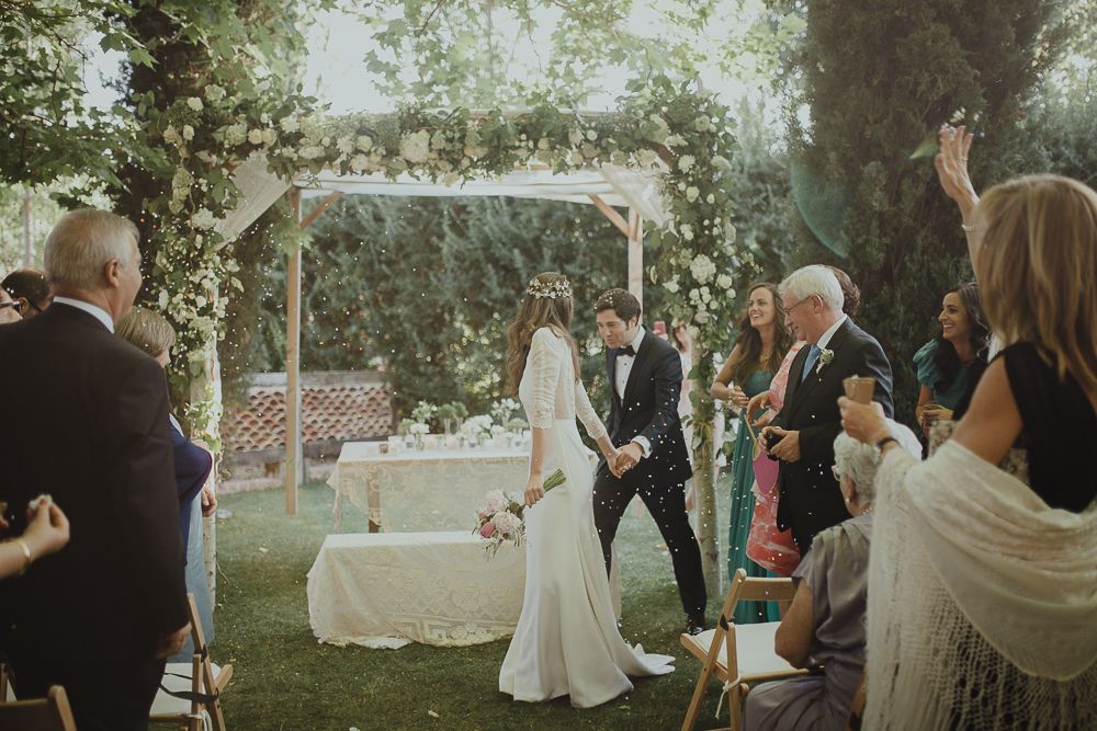 Outdoor garden wedding ceremony with bride and groom at altar surrounded by guests.