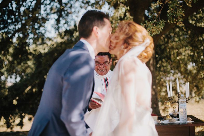 Joyful wedding ceremony moment captured under sunlit trees with champagne glasses in foreground.