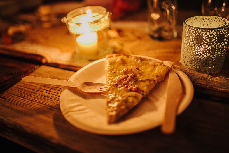 A slice of golden pizza on a white plate illuminated by candlelight during an evening dinner.