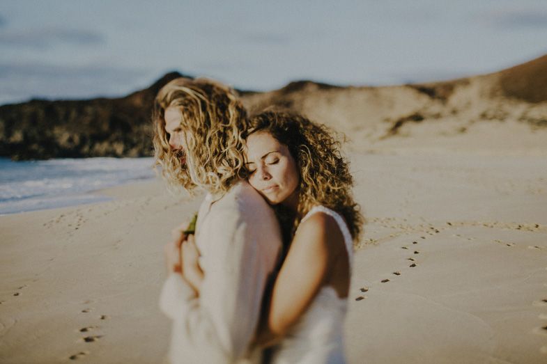 Romantic beach moment with couple embracing on sandy shoreline at sunset.