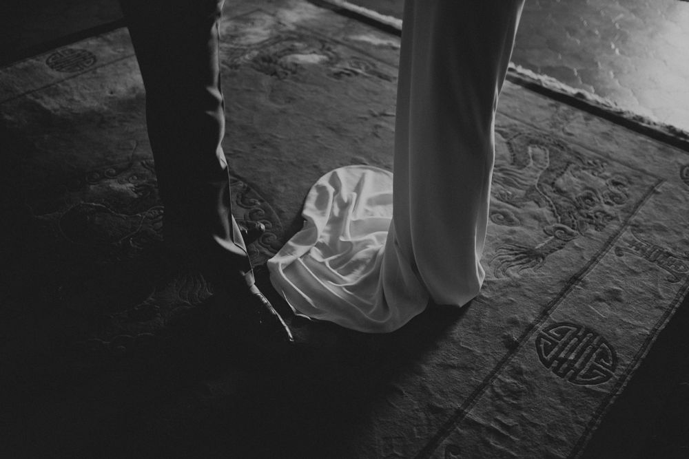 Black and white photo of formal shoes and dress hem on textured ground.