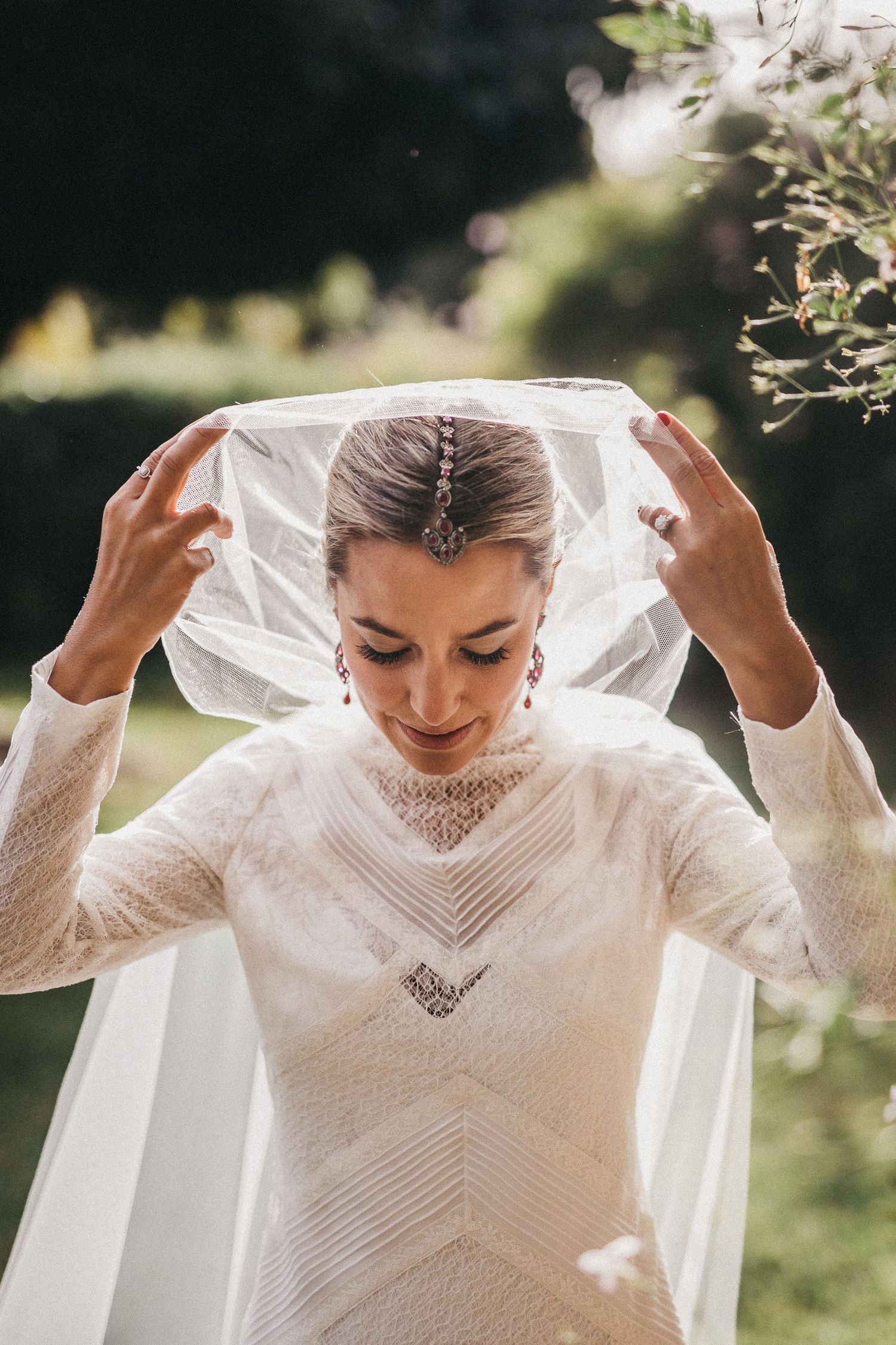 Bride adjusting her delicate veil outdoors, wearing elegant lace wedding dress.