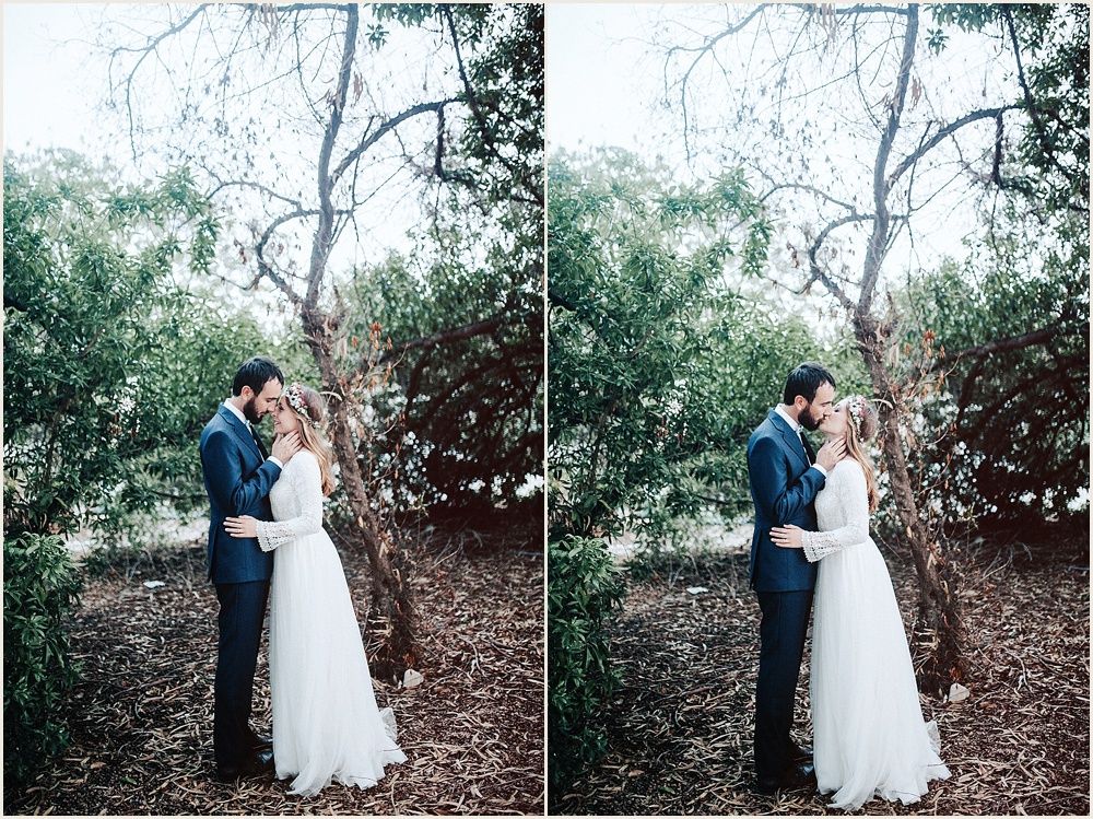 Romantic wedding couple embracing outdoors under tree branches in natural setting.