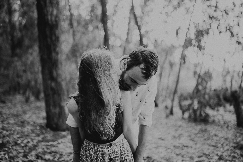 Black and white photo of two people in an intimate moment among trees.