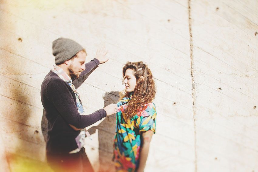 A makeup artist applies cosmetics on a model wearing a colorful tie-dye shirt against a light background.