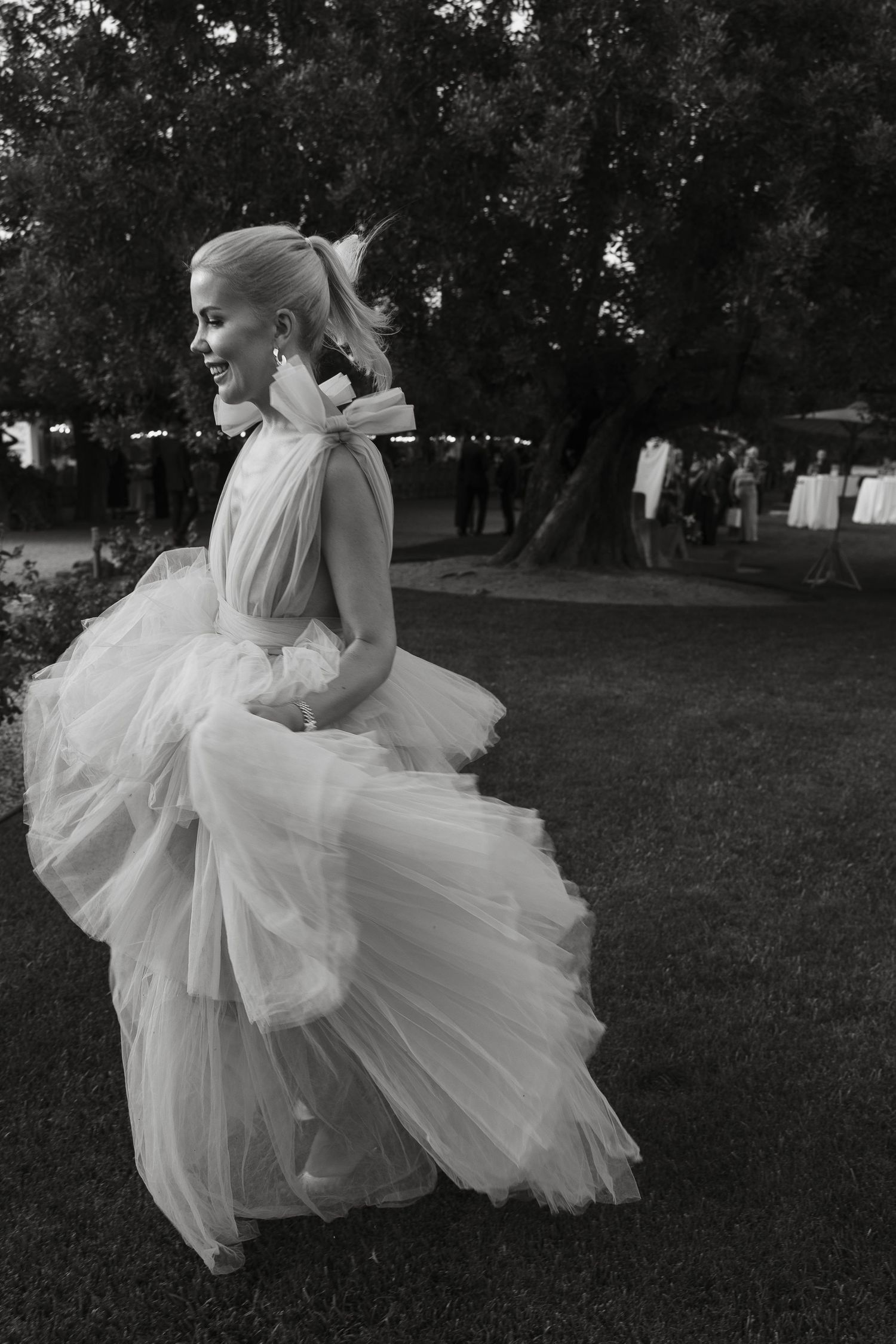 A flowing white tulle gown billows dramatically as its wearer stands in a garden setting.