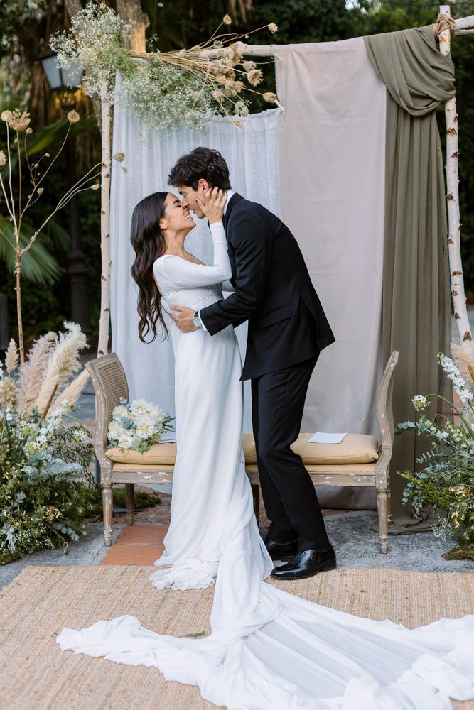 Romantic wedding moment against a floral backdrop with flowing white dress train.