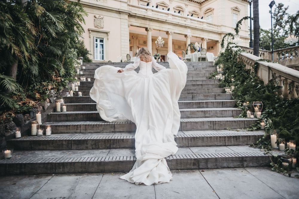 A flowing white wedding dress billows dramatically on grand stone steps of an elegant building.