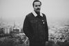 Black and white portrait of person standing against cityscape background.