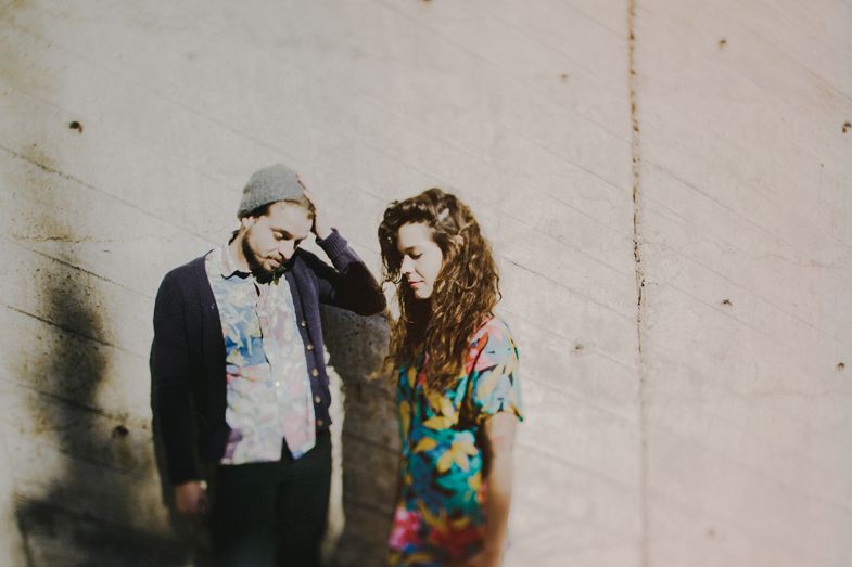 A couple stands close together against a plain wall in vintage-style photography.