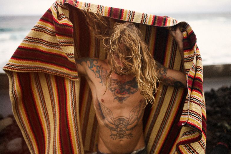 Person wearing striped blanket showing back tattoos against scenic backdrop.