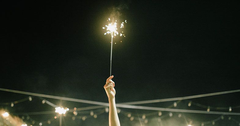 A hand holds a sparkler against a dark night sky during an outdoor celebration.
